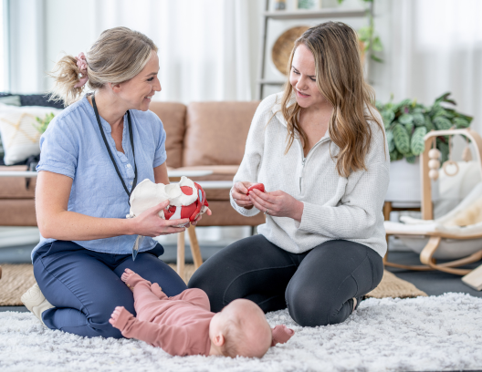 Doctor shows new mother an anatomic model of the pelvis while a baby plays on the floor